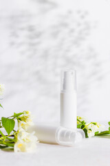 Unbranded skincare products plastic bottle with dispenser and flacons. Tube for cream shampoo. Green jasmine flowers and their shadows on the white background isolated. Mockup and copy space