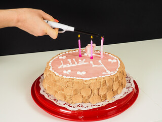Person lighting up candles onto a pink marzipan covered birthday cake, with a rose and decoratet with letters Lily 4