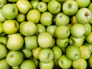 Solid background of green apples in a crate. Many organic Granny Smith apples. Healthy and affordable fruits in the supermarket, source of vitamin C. Pattern for design. View from above.