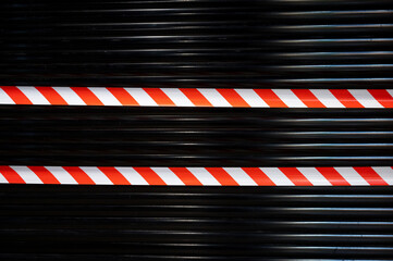 red and white prohibition tape on a black metal roleta. closed during a pandemic in the world....