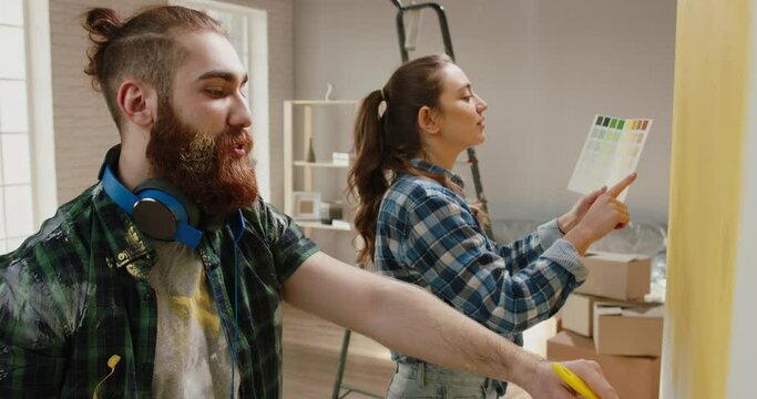 Cute newlywed couple is repairing their new home, painting the walls yellow, positively smiling and enjoying togetherness - new life, young family concept 4k footage