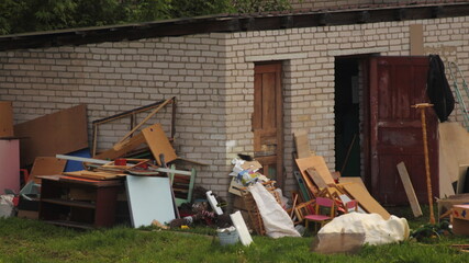 Obraz premium A large pile of old unnecessary things and furniture thrown outdoor next to a abandoned brick barn in the village, General cleaning in the yard on a summer day