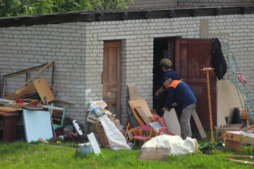 An elderly man and a woman in work clothes are cleaning a brick barn in the village on a summer...