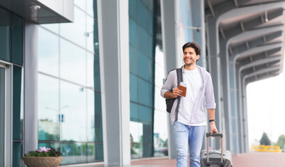 Fototapeta premium Happy man in casual wear walking near airport terminal with luggage