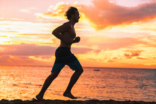 Running man jogging on beach silhouette. Male athlete runner training against sunset training cardio outdoors run. Travel vacation fitness sport.