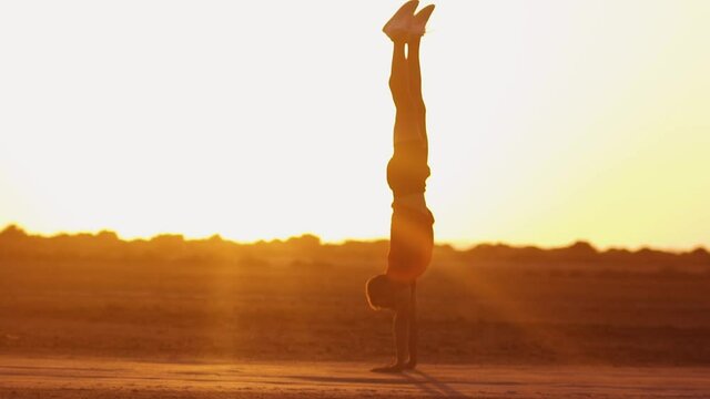 Young sporty man exercising in nature doing handstand at sunset