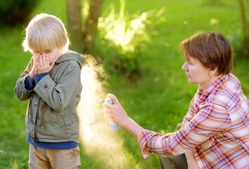 Woman spraying insect or mosquito repellents on little boy before a walk in the forest. Protect children from mosquitoes and other insects.