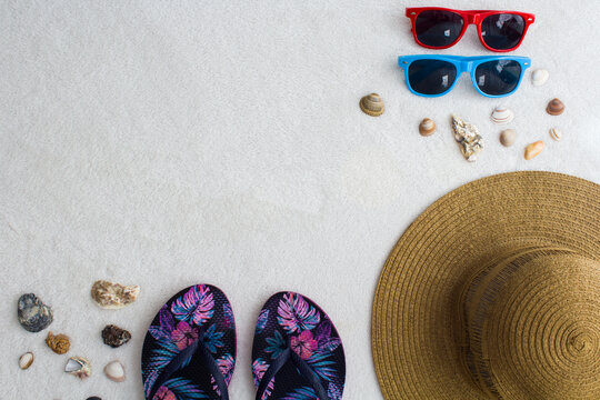 Beach summer objects, straw hat, blue and pink patterned flip flops, red and blue sunglasses, sea snails and space for text.