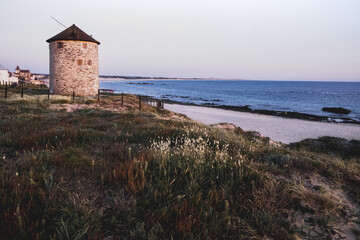 Fototapeta na wymiar Stone windmill view, from a dune, on Apulia beach, Portugal.