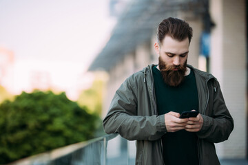 Portrait of outgoing bearded male typing in mobile outdoor