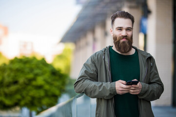 Handsome brutal bearded man is using the phone on the street