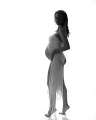 Black and white romantic image of a pregnant woman in white fabric. Pregnancy and expecting a baby concept