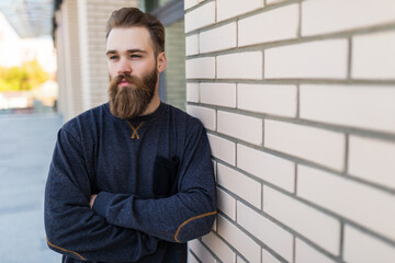 Young bearded hipster man near brick urban wall background.