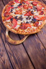 Italian pizza with pepperoni, tomatoes, olives and basil on wooden table. Top view with copy space