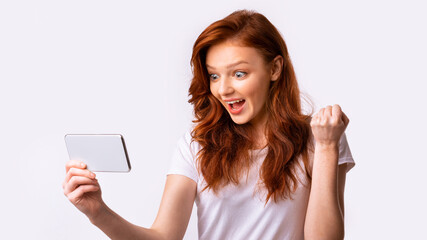 Fototapeta premium Girl With Smartphone Gesturing Yes Winning Game Over White Background