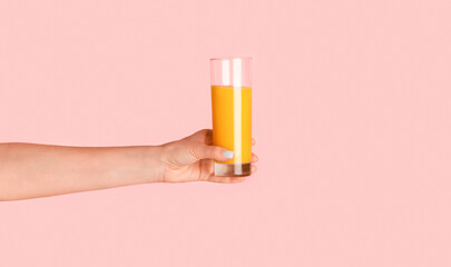 Close up of girl hand holding glass of orange juice on pink background, panorama