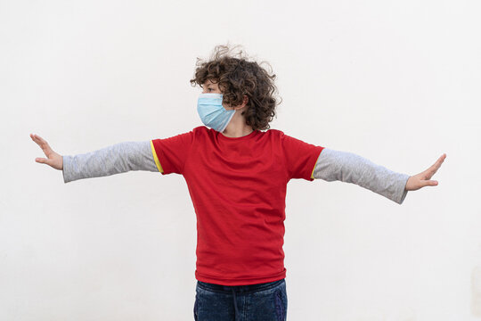 An 8 year old boy wearing a coronavirus face mask spreads his arms to indicate the minimum social distance of one meter (6 feet).