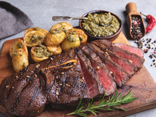 Sliced juicy grilled steak medium rare beef on bone roasted potatoes sauce pesto