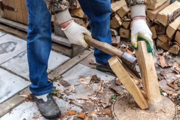 A man in gloves and blue jeans cut in half a birch log with an ax with a wooden handle. Logging firewood for the fireplace.