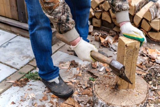 A man in gloves and blue jeans cuts and cleans birch firewood with an ax with a wooden handle, with which a fireplace, stove or a fire will be heated.