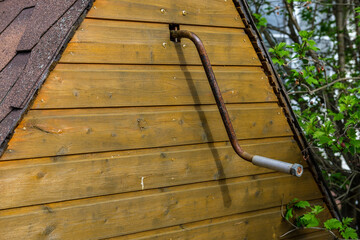 Rusty handle (gate) of a well for lifting water with a bucket. House over the well painted in the old style in yellowish shades.
