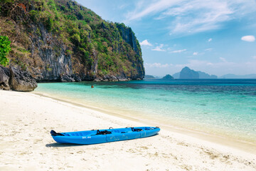 A blue kayak lies on white sand surrounded by mountains. Tropical beach with crystal clear water.