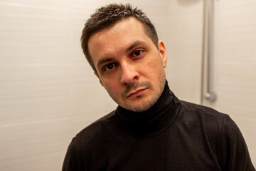 Portrait of a young short haired man wearing black turtleneck on background of light and looking at camera.