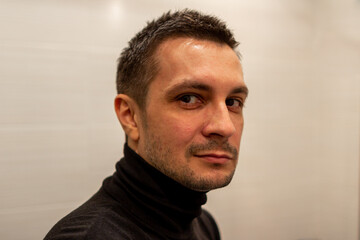 Fototapeta premium Portrait of a young short haired man wearing black turtleneck on background of light and looking at camera.