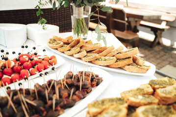 Self-service buffet table with various types of small snacks. Focused on baguette smeared with basil pesto. Celebration, birthday, party, wedding