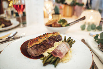 Meal served on festive table. Piece of beef meat with mashed potatoes and green bean pods on white plate. Celebration, party, birthday or wedding