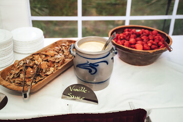 Sweet snack. Jug of vanilla sauce and bowl of fresh strawberries on self-serving buffet table. Celebration, party, birthday or wedding concept.