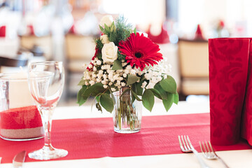 Festive table decoration. Close up of colorful flower bouquet in glass vase and arrangement of glassware and cutlery. Celebration, wedding, birthday