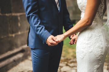Young adult groom and bride holding hands. Outdoor photo. Wedding day concept.