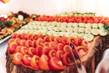 Sliced fresh tomato and cucumber laying on wooden board on buffet table for vegetable garnish to main dish. Celebration, party, birthday or wedding