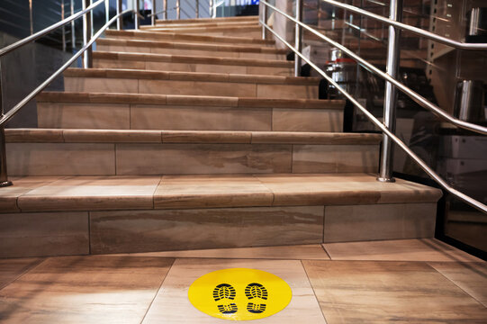yellow sticker on the floor in front of the stairs indicating the need to keep a distance during a pandemic. keep distance in a public place