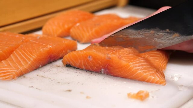 Cutting raw salmon fillet on a white chopping board. Preparing fish steak for cooking in the kitchen.