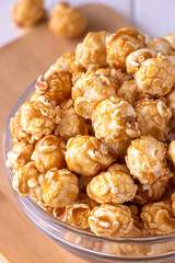 Sweet caramel popcorn in glass bowl. Close up. Light wooden background.