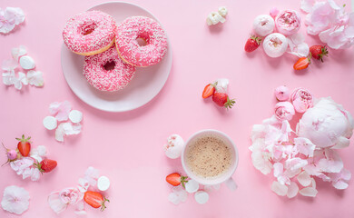 Top view composition of three donuts with icing on a pink plate, cup of cofee, strawberries and pink flowers on a pastel pink background. Festive concept.