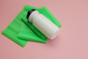 online sports at home, during self-isolation,keep the figure in shape, on a pink background is a green elastic band for exercise, a white water bottle