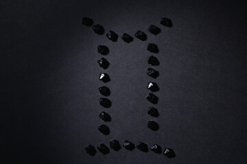 Symbol of the zodiac sign Gemini made by black stones on a black background. Low dark key