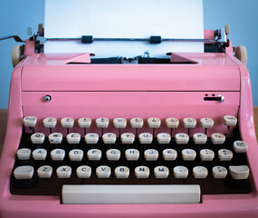 A vintage pink typewriter and paper is ready for typing