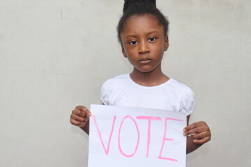 Girl holding white paper sign with the word Vote written in pink letters