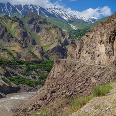 Road in a deep mountain gorge. Below is a tumultuous river Panj. Pamir Highway, Tajikistan. On the opposite bank of the territory of Afghanistan.