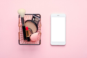 Buy cosmetic online via mobile phone app concept. Flat lay composition with shopping cart with...
