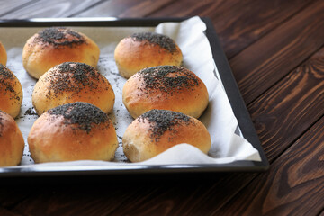 Fresh homemade burger buns with poppyseed, concept of burger and homemade food. Mini challah. Homemade bread on paper patchment and tray on wooden background