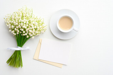 Envelope with blank paper note mockup, cup of coffee and lily of the valley flowers on white background. Wedding invitation card, love letter, romance concept.