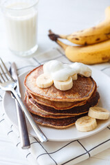 Banana pancakes with whole wheat flour on white background, bananas, yogurt and glass of milk. Healthy breakfast, morning concept