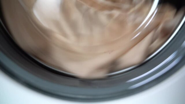 Closeup bottom of the glass door of the washing machine. Clothes rotate counterclockwise in a chrome drum from right to left