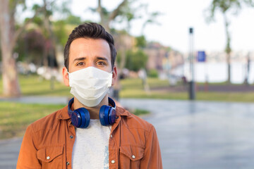Portrait of young man wearing medical mask posing in sunny park