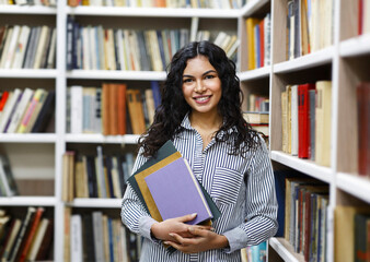 Smiling latina girl holding textbooks at library